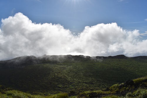 三原山山頂付近からカルデラの縁を望む。（カルデラの縁では、海から吹き上げる風によって雲が作られている）
